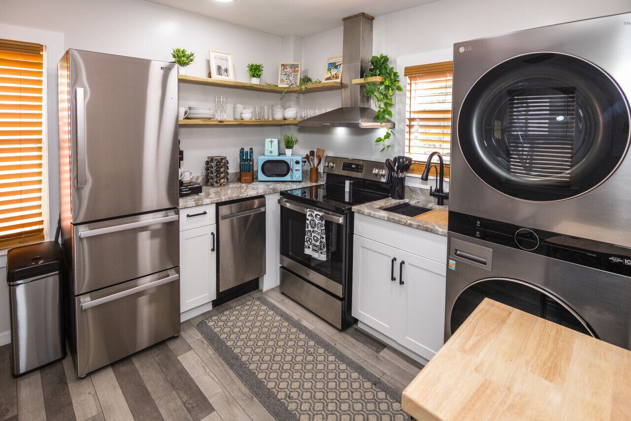 A modern kitchen with stainless steel appliances, white cabinetry, and a built-in washer and dryer.