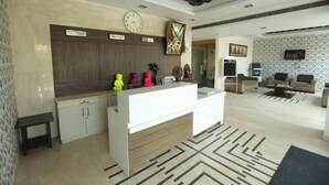 A modern reception area with a reception desk, a clock, and a patterned wall. - Hotel Grand Tushar Elegant (Ghaziabad)