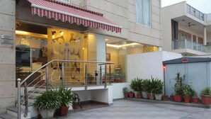 A hotel entrance with a red awning, a staircase, and potted plants. - Hotel Grand Tushar Elegant (Ghaziabad)