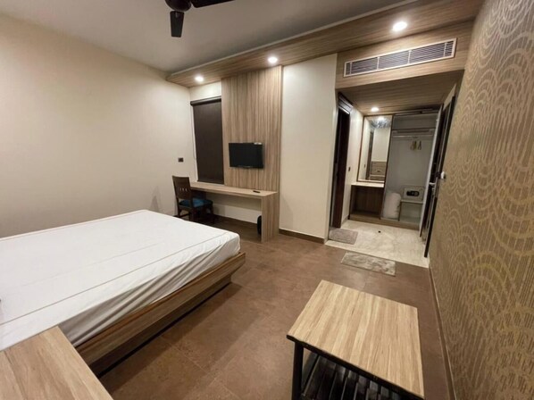 A modern bedroom with a bed, a desk, a TV, and a bathroom visible through an open door. - Hotel Grand Tushar Elegant (Ghaziabad)