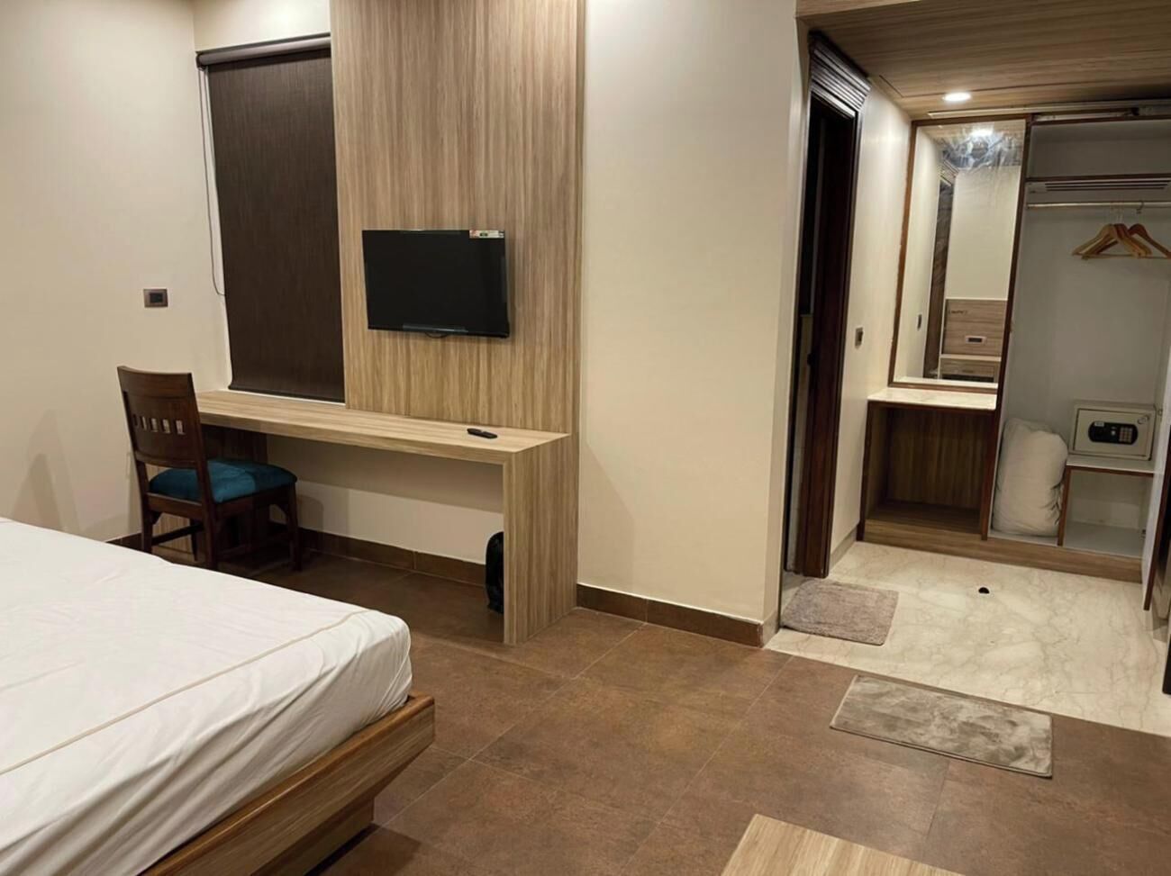 A bedroom with a bed, a desk, a chair, a television, a wardrobe, and a mirror.