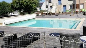 Una piscina rectangular amb un solàrium de fusta, envoltada de mobiliari de vimet i una tanca de seguretat.