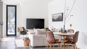 Een moderne woonkamer met een bank, een eettafel met stoelen, een televisie en een plant.