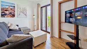 Una sala de estar moderna con un sofá, una mesa de centro, un televisor de pantalla plana y una puerta a un balcón.