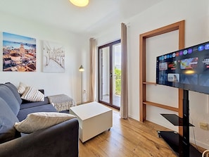 Ein modernes Wohnzimmer mit einer Couch, einem Couchtisch, einem Flachbildfernseher und einer Balkontür.