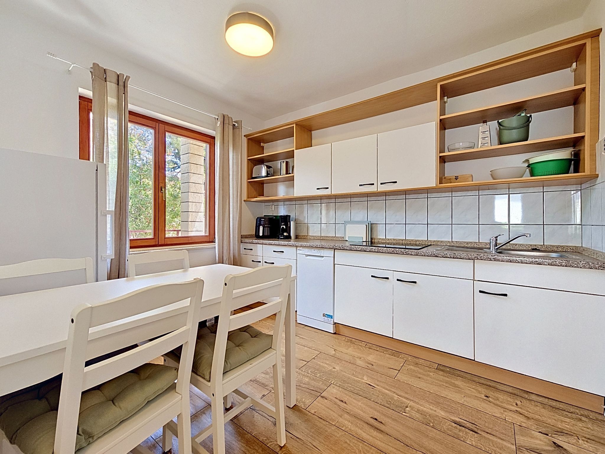 A kitchen with white cabinets, a wooden countertop, and a window with curtains.