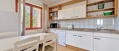 A kitchen with white cabinets, a wooden countertop, and a window with curtains.