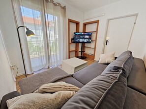A living room with a grey sofa, a flat-screen TV, a standing lamp, and a window with sheer curtains. - Dalero 1 by Interhome (Trogir/Okrug Gornji)