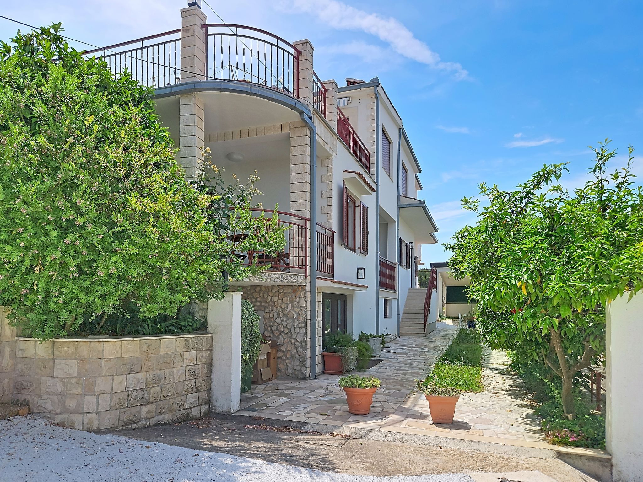 Ein mehrstöckiges Wohnhaus mit einem gebogenen Balkon, Steinwänden und Pflanzgefäßen entlang des Weges.
