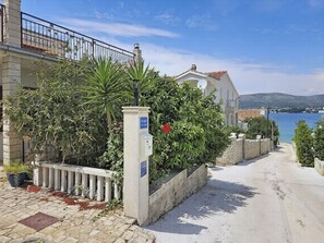 Una strada costiera con un muro di pietra, un cancello in metallo e un edificio con un'antenna parabolica.
