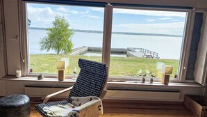 A room with a large window overlooking a lake, a chair with a blanket, a small table with a lamp, and a wooden floor. - Havstomten by Interhome (Blekinge)