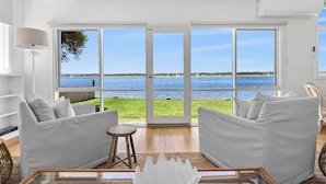 Quarto com uma grande porta de vidro deslizante que dá para o mar, dois sofás listrados, um banquinho de madeira e uma mesa de centro de vidro.