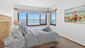 Quarto com uma cama, um abajur, um quadro e vista para o mar.