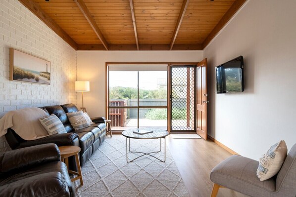 Ein gemütliches Wohnzimmer mit einer Ledersofa, einem grauen Sessel, einem Couchtisch und einem an der Wand befestigten Fernseher.