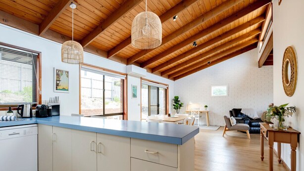 Tilava keittiö, jossa on suuri keittiösaareke, puupalkit katossa ja riippuvalaisimet.