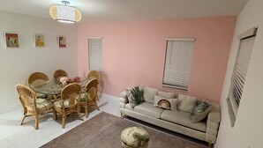 Un salon avec une table ronde en verre entourée de chaises en osier, un canapé beige agrémenté de coussins décoratifs et un tapis marron.