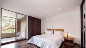 A modern bedroom with a large bed, wooden flooring, a glass door leading to a balcony, and a hammock. -  Apartamentos Casa Grande (Rionegro)