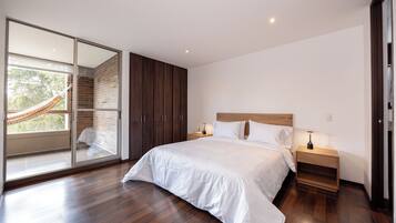 A modern bedroom with a large bed, wooden flooring, a glass door leading to a balcony, and a hammock.