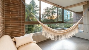 A room with a brick wall, large windows, a hammock, and a sofa with pillows. -  Apartamentos Casa Grande (Rionegro)