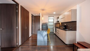 A modern kitchen with a central island, wooden cabinets, and a bar stool. -  Apartamentos Casa Grande (Rionegro)