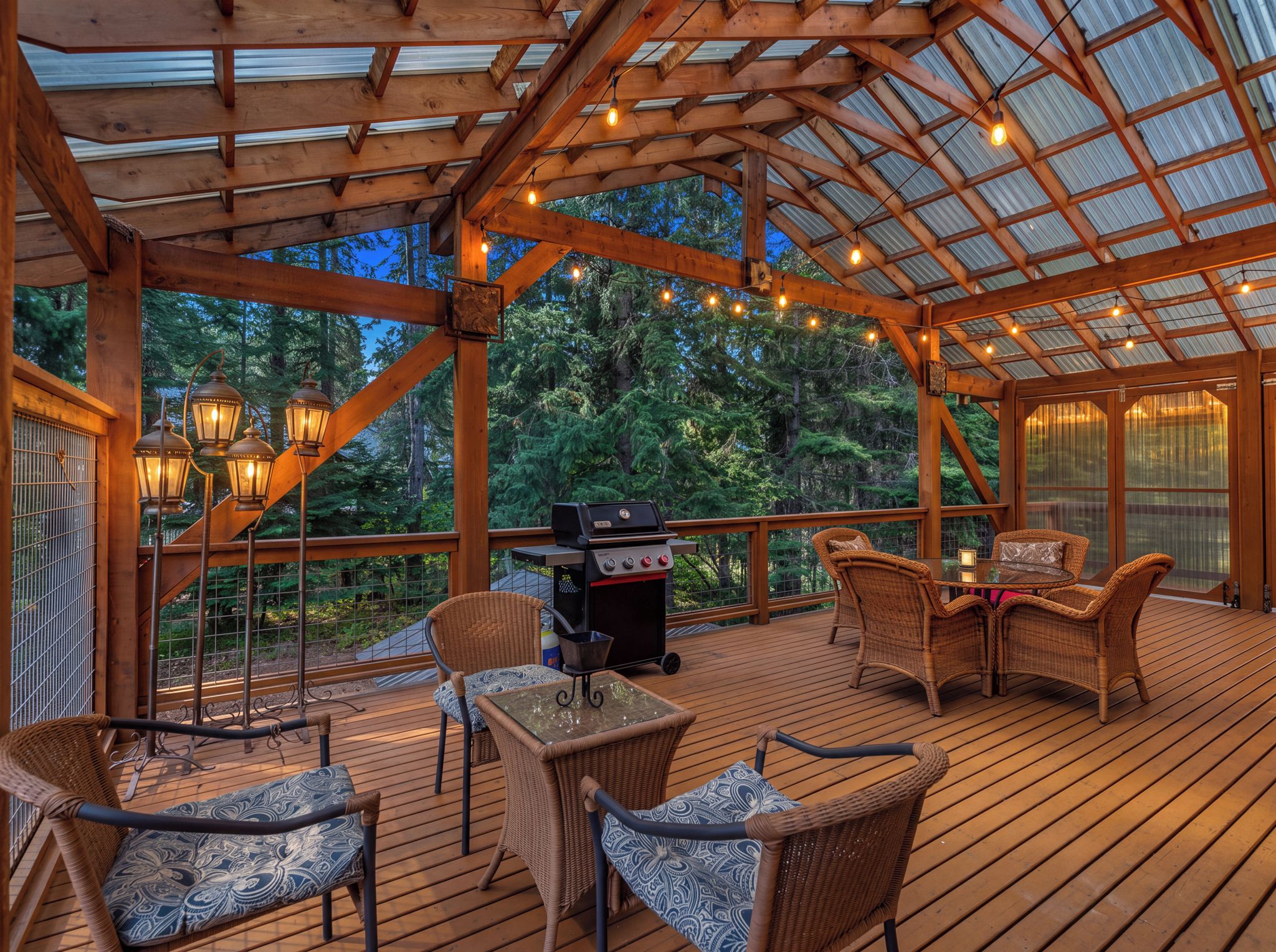 An outdoor deck with wooden flooring, wicker furniture, a grill, and string lights.