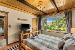 Una habitación tipo cabaña con una cama, un televisor, un ventanal con vista al bosque y un cartel en la pared.