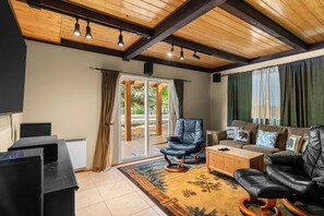 Un salón espacioso con un sofá de cuero negro, una mesa de centro de madera y un sillón de cuero negro. Un ventanal corredero da a un área exterior.