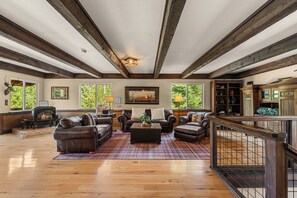 A spacious living room with a fireplace, leather sofas, a coffee table, and a view of the outdoors through large windows. - 4BR Mountain Escape - Covered Hot Tub, Deck, near River (Leavenworth)