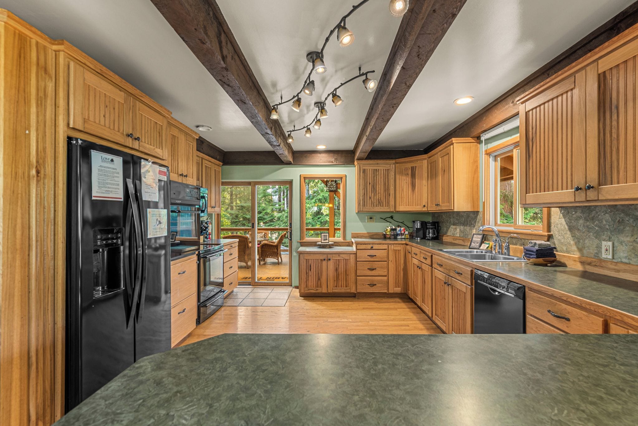 A modern kitchen with wooden cabinets, a black refrigerator, and a stone countertop.