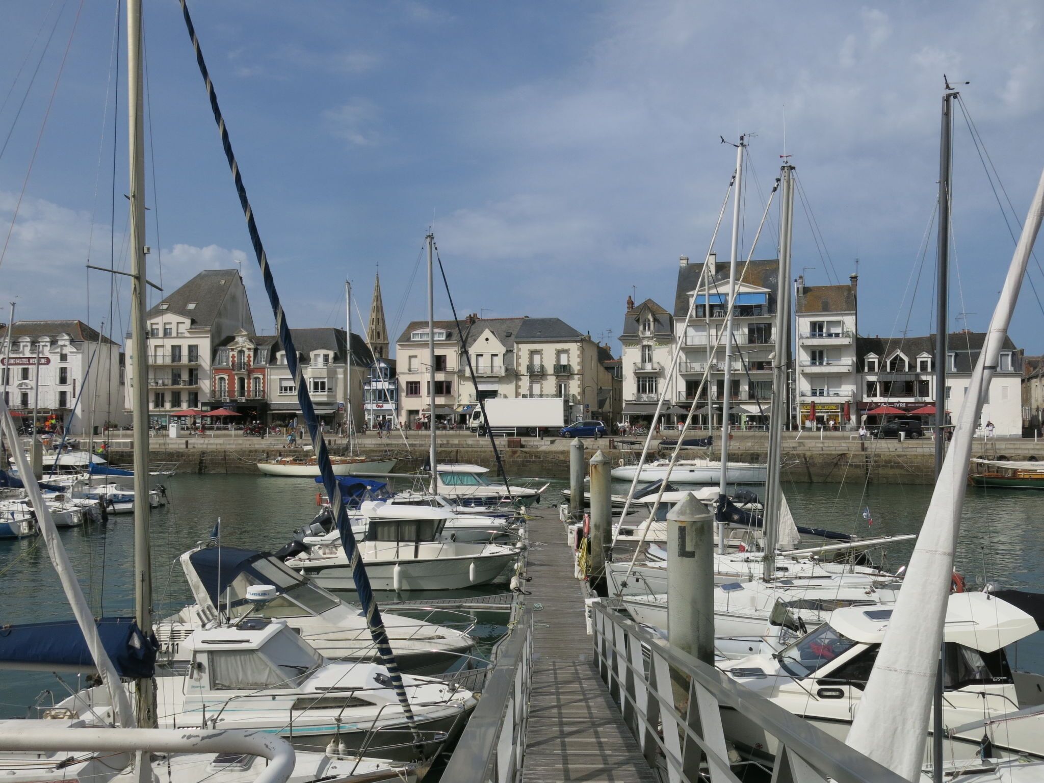 Un puerto deportivo con barcos amarrados, un muelle de madera y edificios con balcones al fondo.