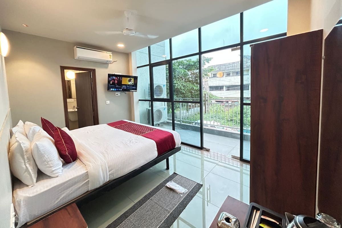 Een moderne hotelkamer met een bed, een televisie, een airconditioningsysteem en een balkon met uitzicht op de stad.
