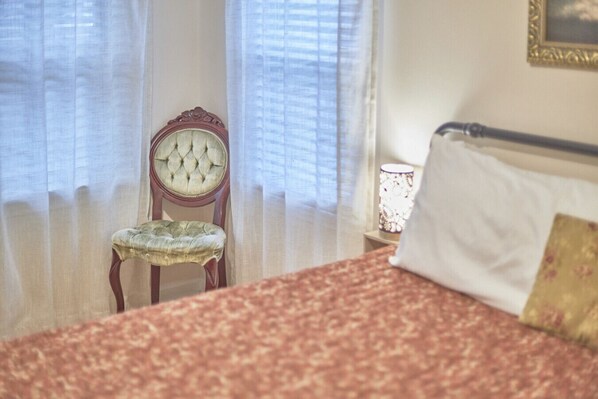 A bedroom with a bed, a chair, and a nightstand with a lamp.