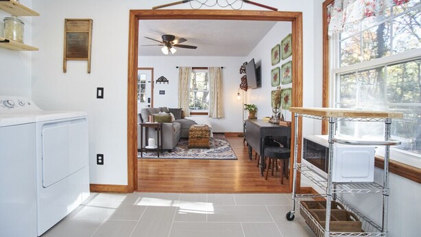 A laundry area with a washing machine, a ceiling fan, and a wooden door leading to a living room with a sofa, a coffee table, and a dining area with a table and chairs. - Newly remodeled 2BR in Chapel Hill (Chapel Hill)