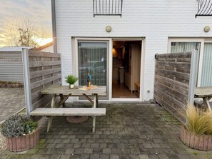 A white building with a wooden fence, a patio with a table and benches, and a small garden area. - Tureluur II with terrace by Interhome (Bredene)