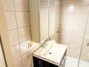 A modern bathroom with a large mirror, a white sink, and a shower area. - Tureluur II with terrace by Interhome (Bredene)