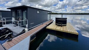 A modern floating house with a dock, a hot tub, and a clear view of the lake.