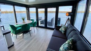A modern interior with a dining area, a sofa, and large windows offering a view of the water.