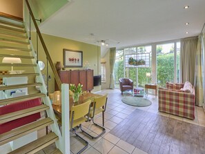 A spacious living area with a staircase, a dining table with chairs, a sofa, and a large window offering a view of greenery. - Wellness and tranquillity in green Twente (Oldenzaal)