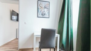 Une pièce avec un bureau blanc, une chaise grise, une œuvre d’art encadrée au mur et un rideau vert.