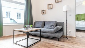 Une pièce moderne avec un canapé gris, une table basse en bois et un lampadaire. Trois petites images encadrées sont accrochées au mur.