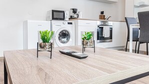 Une cuisine moderne équipée d’un four à micro-ondes, d’une machine à café et d’un lave-linge. Deux plantes en pot sont posées sur la table à manger.