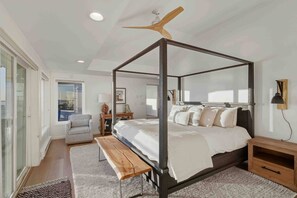 Ein modernes Schlafzimmer mit einem Himmelbett, einem Deckenventilator, einer Bank und Blick ins Freie.