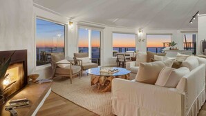 Un salon spacieux doté d’une grande fenêtre offrant une vue sur le coucher de soleil, d’une cheminée et d’un coin salon confortable.