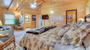 A wooden cabin bedroom with a bed, a desk, a chair, a ceiling fan, and a television. - Resort-Style Smokies Cabin w/ Hot Tub + Game Room (Pigeon Forge)