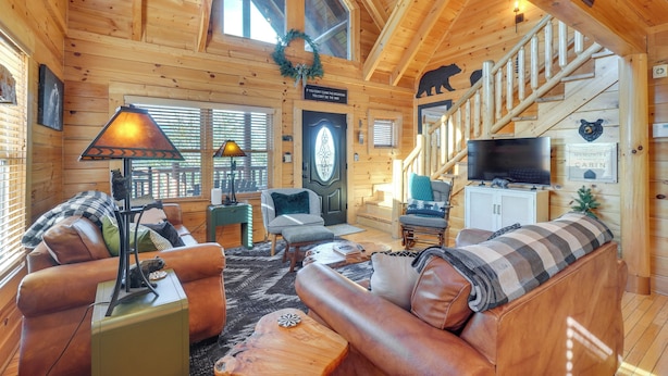 A cozy cabin interior with wooden walls, a fireplace, a sofa, and a television. - Resort-Style Smokies Cabin w/ Hot Tub + Game Room (Pigeon Forge)