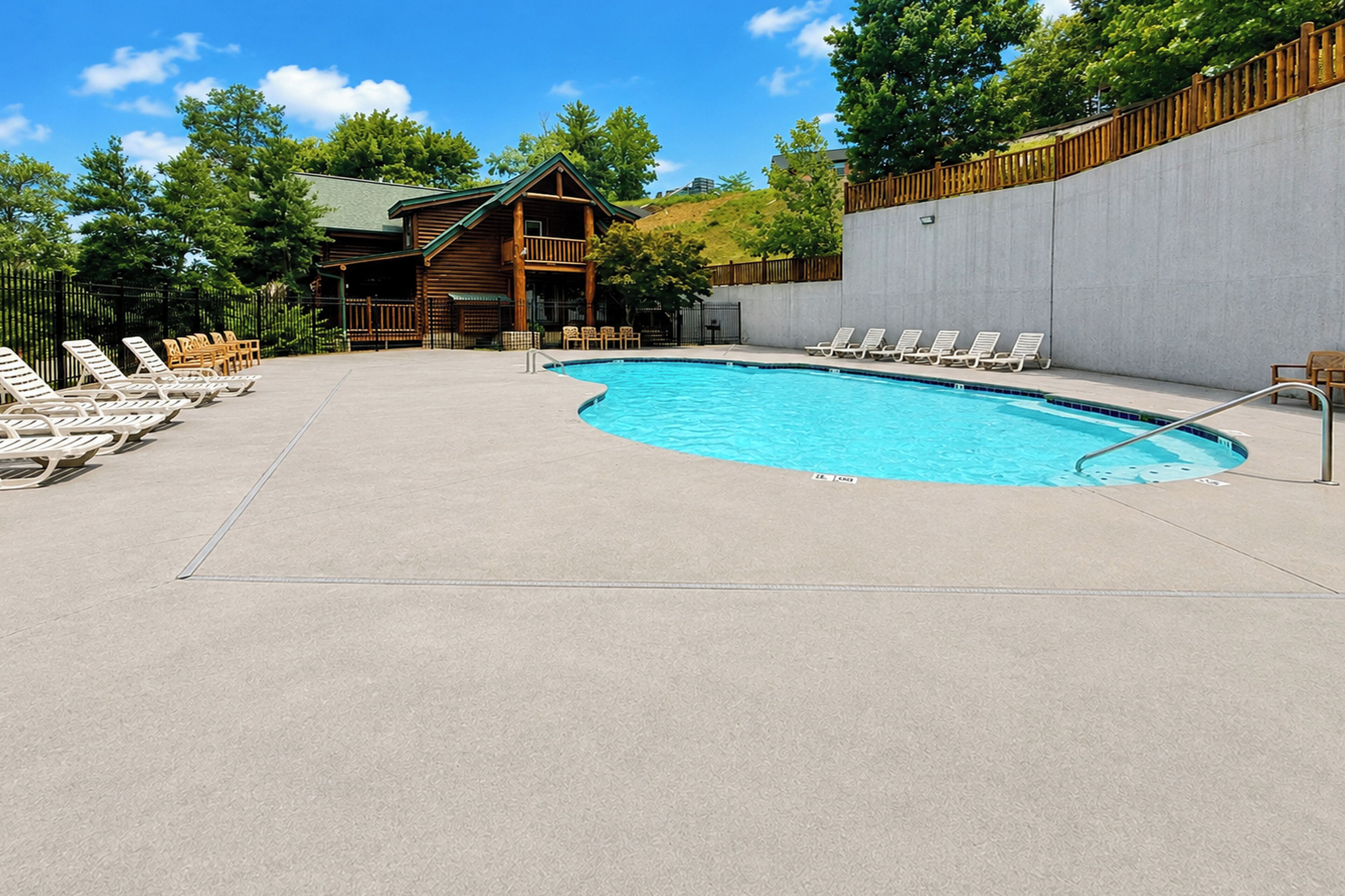 A swimming pool with lounge chairs, a wooden building, and a concrete wall.