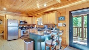 A spacious kitchen with wooden cabinets, stainless steel appliances, and a large island with bar stools. - Resort-Style Smokies Cabin w/ Hot Tub + Game Room (Pigeon Forge)