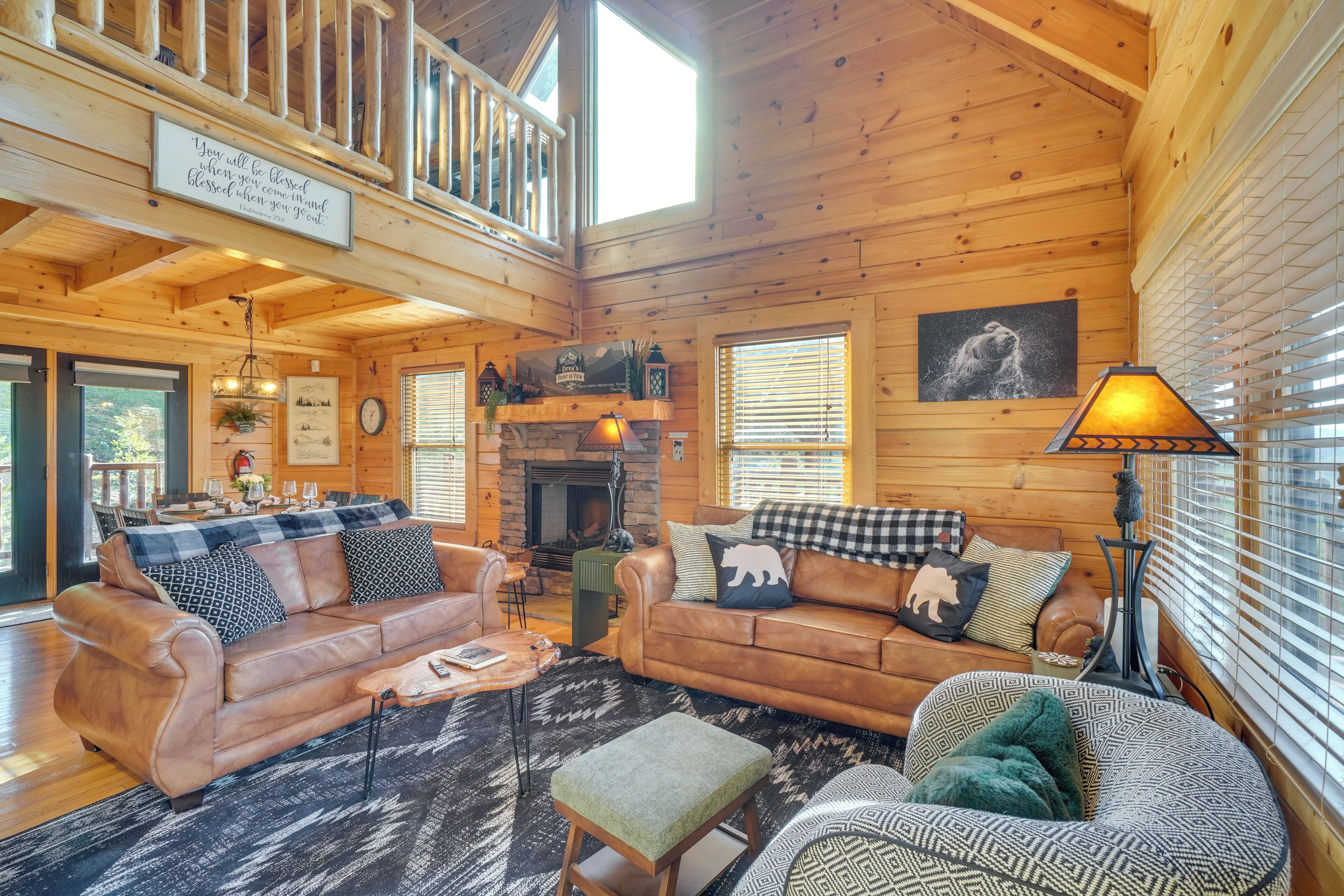 A cozy cabin interior with a fireplace, leather sofas, a dining area, and a balcony.
