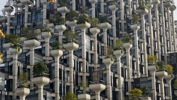 Ein modernes Gebäude mit einem einzigartigen architektonischen Design und mehreren hervorstehenden Balkonen mit Bepflanzung.