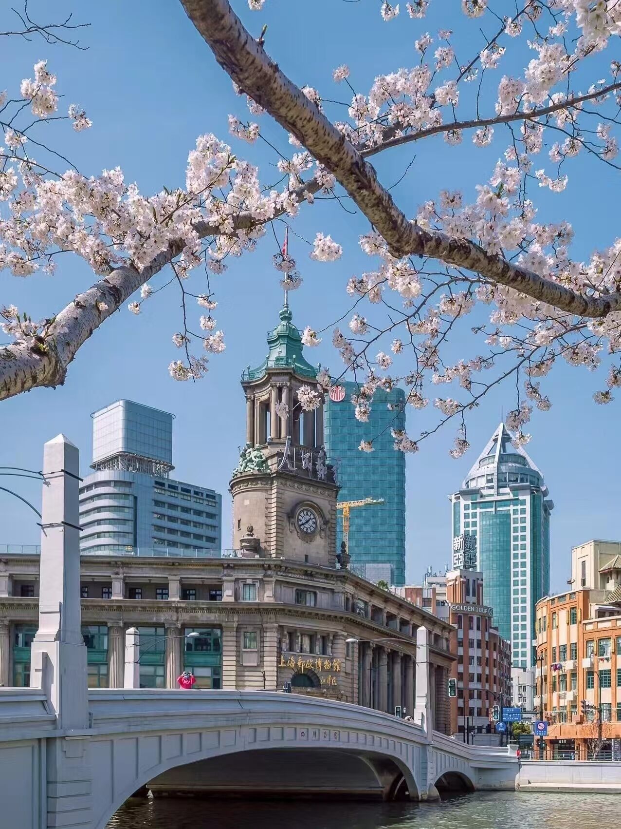 A bridge with a clock tower and a building with a green roof in the background.
